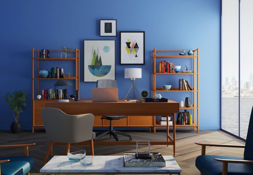 Modern office with a wooden desk, shelves filled with books and decor, blue walls, framed artwork, and a large window overlooking a cityscape—ideal inspiration for your next home renovation.