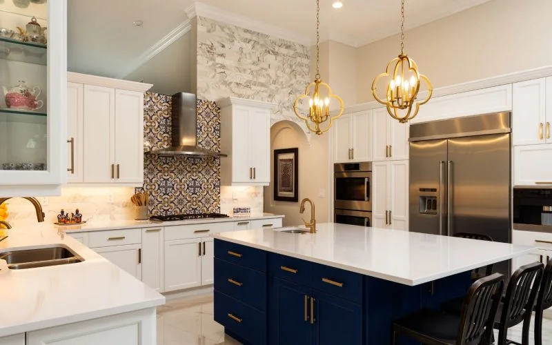 Modern kitchen with white cabinets, a blue island, stainless steel appliances, decorative tile backsplash, and two gold pendant lights.
