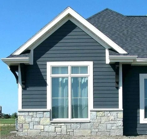 A house exterior with dark gray horizontal siding, white trim, stonework at the base, and a large window under a gable roof.
