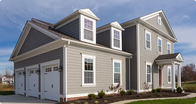 Two-story suburban house with gray siding, white trim, and a three-car garage. The front yard has minimal landscaping and a concrete driveway.