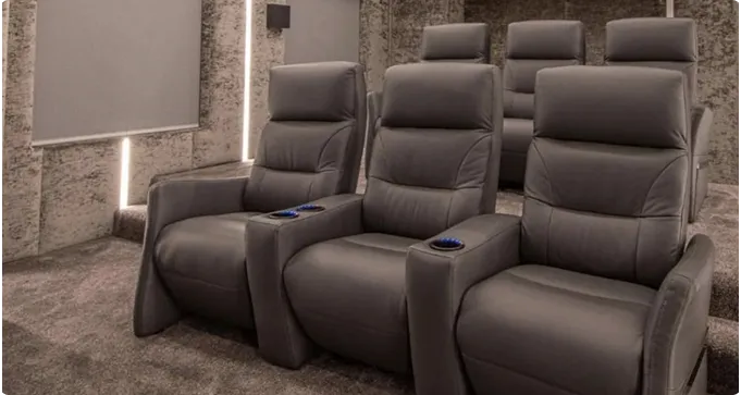 A home theater room with two rows of gray recliner seats, cup holders in the armrests, and carpeted floors and walls.