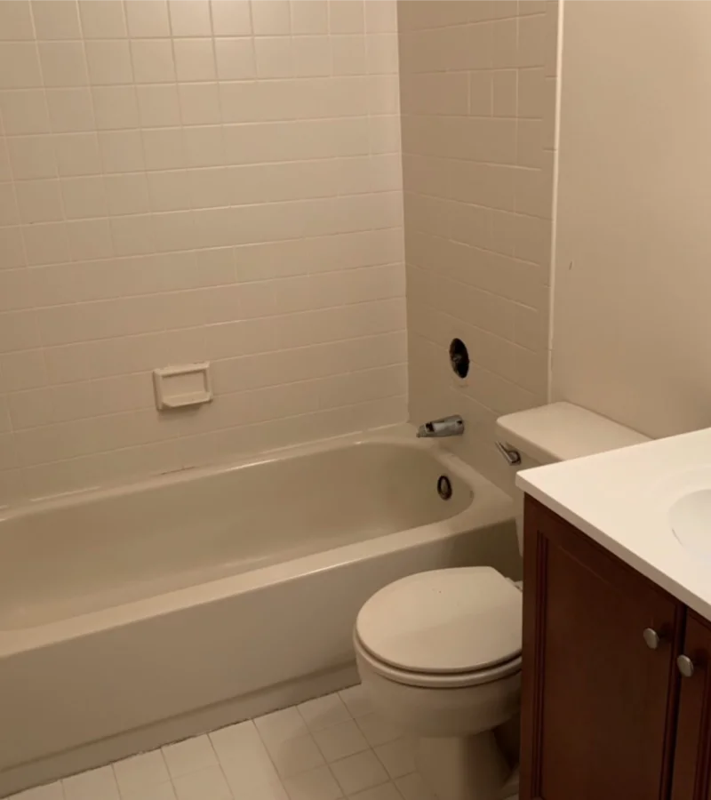 A bathroom with a white bathtub, a toilet, and a vanity with a sink. The walls and floor are tiled in white.