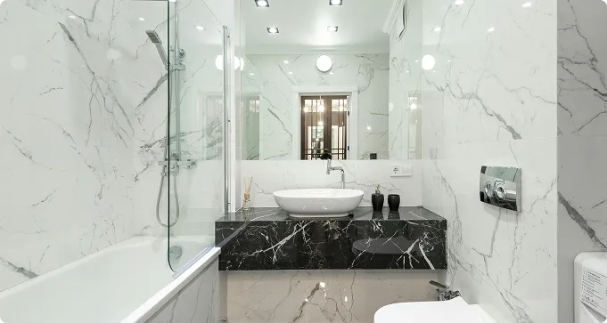 Modern bathroom with marble walls and floor, a bathtub with glass screen, black marble vanity with a white vessel sink, and a large mirror above the sink.