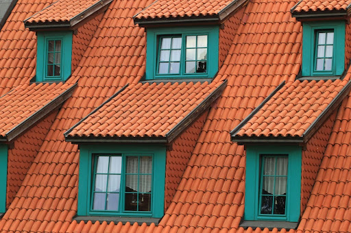 A close-up view of a red tiled roof with multiple green-framed dormer windows.