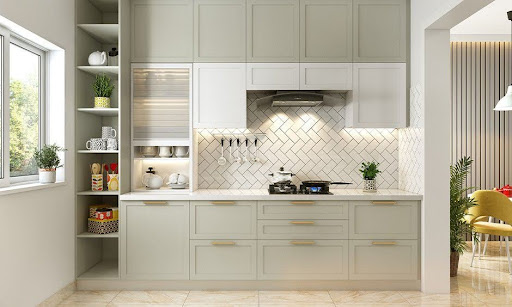 Modern kitchen with light green cabinets, white backsplash in herringbone pattern, gas stove, open shelves, and sunlight coming through a window on the left.