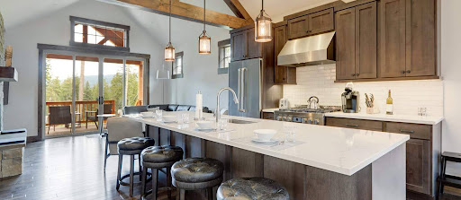 Modern kitchen with dark wood cabinets, stainless steel appliances, a large island with barstools, and pendant lighting; open living area with large windows and mountain view.