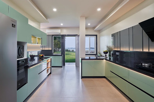 Modern kitchen with mint green cabinets, black countertops, built-in appliances, and large windows overlooking a grassy outdoor area.