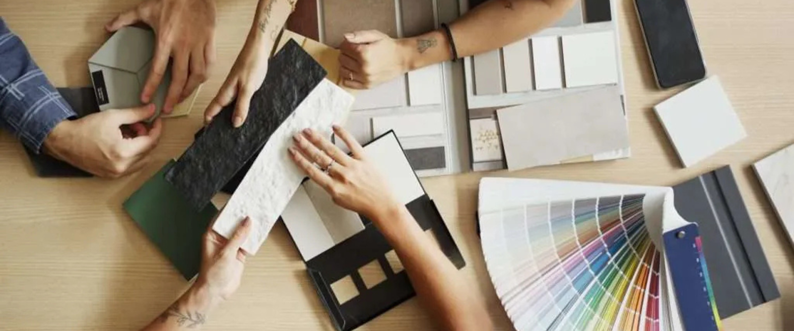 Four people select materials and color swatches from various samples and palettes on a table, possibly for interior design or renovation planning.