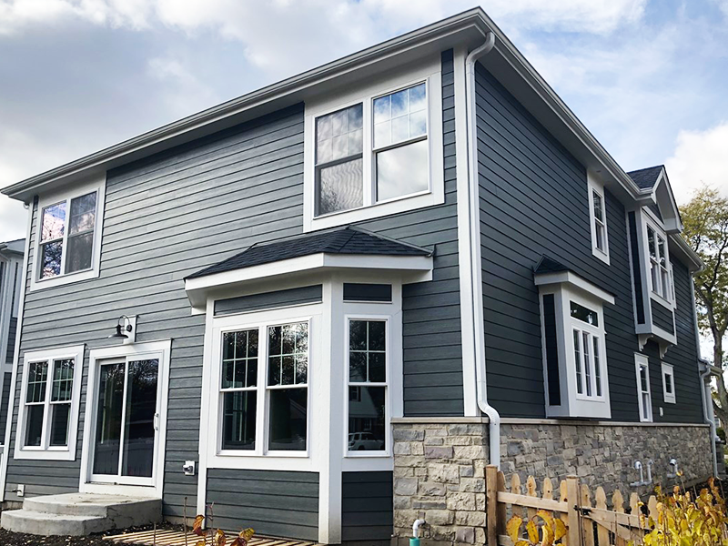 Two-story modern house with gray horizontal siding, white trim, multiple large windows, and a stone accent on the lower exterior—perfect inspiration for anyone considering home remodeling in Lynbrook.