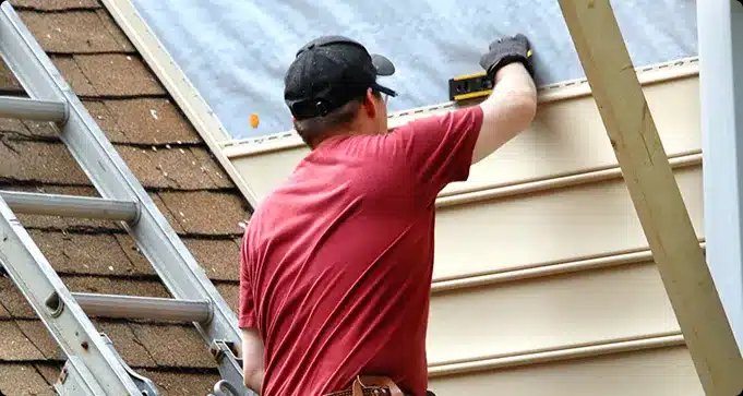 Worker installing exterior siding beside a ladder